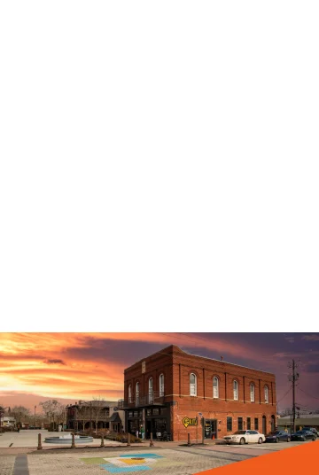 Gritz Brunch Bar in O'Neal Plaza with metal benches, bare winter trees, green plants, curved light posts, cars on the street, and clouds at sunset Cheap car insurance in Douglasville, Georgia.