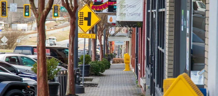 Gray brick sidewalk with bare winter trees, shops, restaurants, bars, and parked cars along the street on a cloudy day in Douglasville, Georgia: Cheap car insurance in The Peach State.