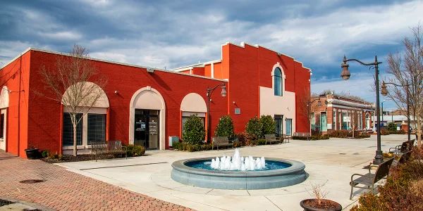 Gritz Brunch Bar in O'Neal Plaza with metal benches, bare winter trees, green plants, curved light posts, cars on the street, and clouds at sunset Cheap car insurance in Douglasville, Georgia.