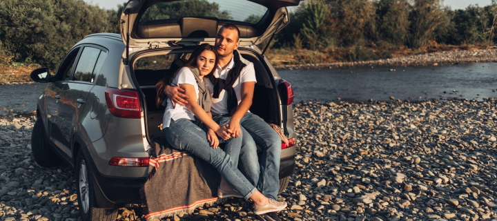 Happy Couple on Road trip into the Sunset in SUV Car.